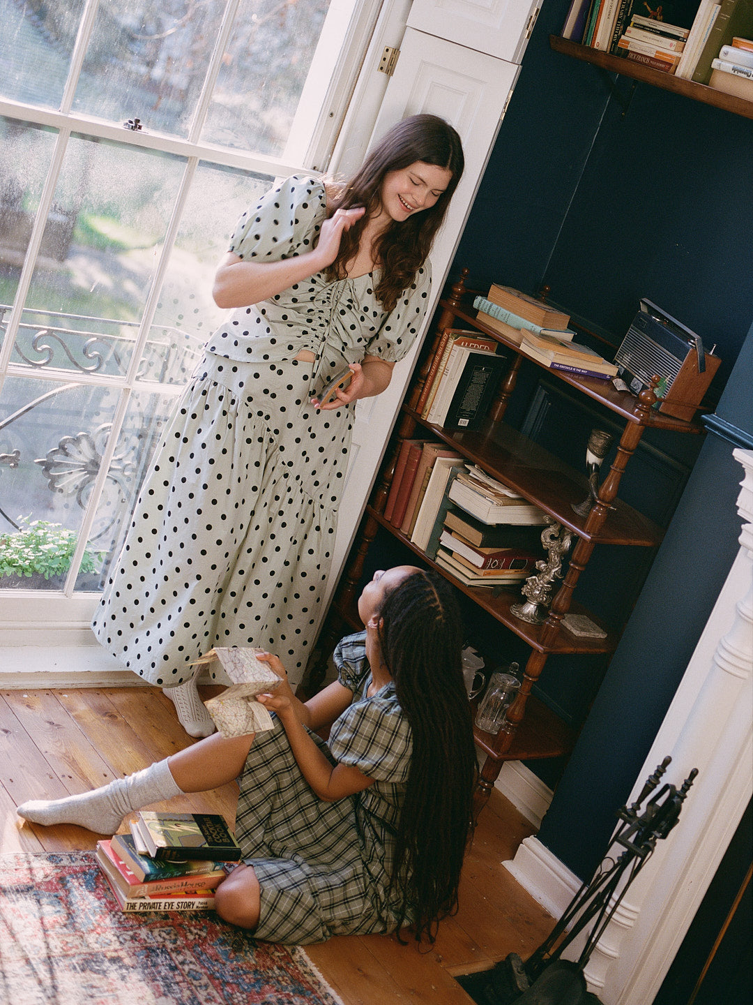 Two women in a cozy room with books and a window.